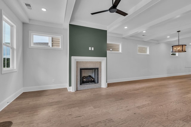 unfurnished living room with a wealth of natural light, a tile fireplace, wood finished floors, and beam ceiling