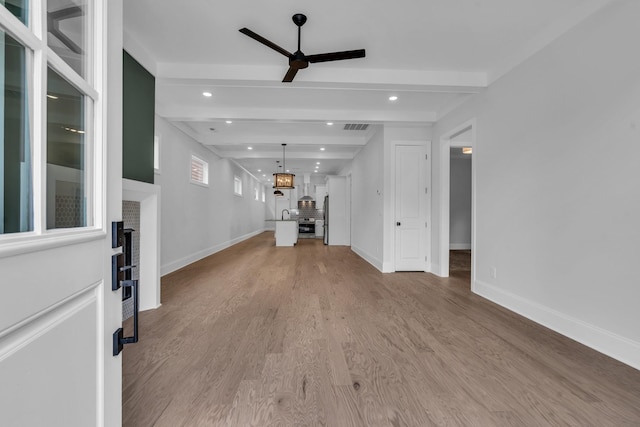 unfurnished living room with a ceiling fan, beamed ceiling, light wood-style flooring, and baseboards