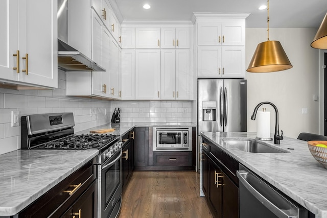 kitchen with wall chimney range hood, white cabinetry, stainless steel appliances, and a sink