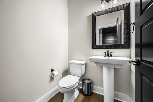 half bathroom with wood finished floors, toilet, and baseboards