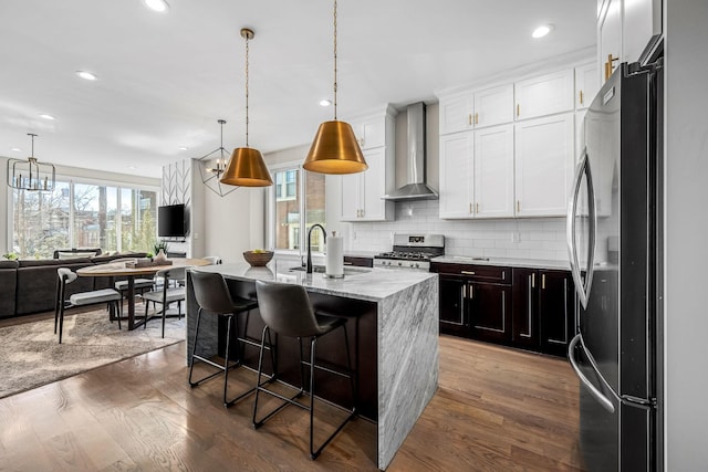 kitchen featuring open floor plan, stainless steel range oven, wall chimney range hood, freestanding refrigerator, and an island with sink