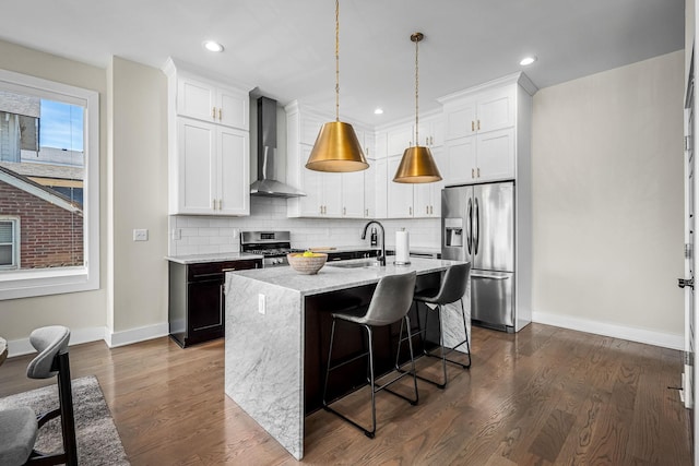 kitchen featuring wall chimney exhaust hood, appliances with stainless steel finishes, an island with sink, and white cabinets