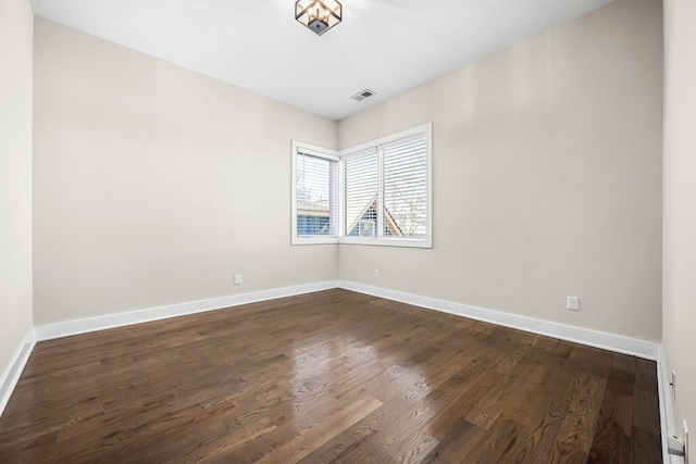 spare room with baseboards, visible vents, and dark wood finished floors