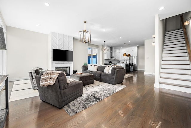 living room with recessed lighting, dark wood-type flooring, stairs, a glass covered fireplace, and an inviting chandelier