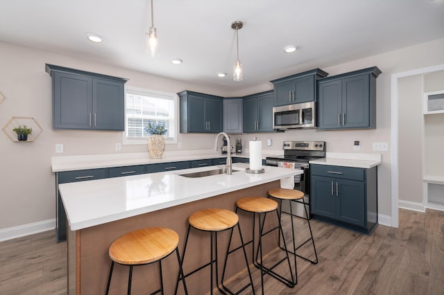 kitchen featuring a breakfast bar, stainless steel appliances, light countertops, a kitchen island with sink, and a sink