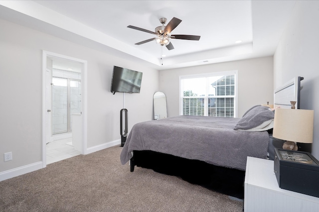 bedroom with a raised ceiling, ensuite bathroom, light carpet, ceiling fan, and baseboards