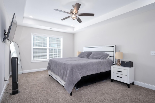 bedroom featuring light carpet, baseboards, a tray ceiling, and ceiling fan