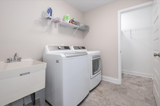 clothes washing area with a sink, laundry area, washing machine and clothes dryer, and baseboards