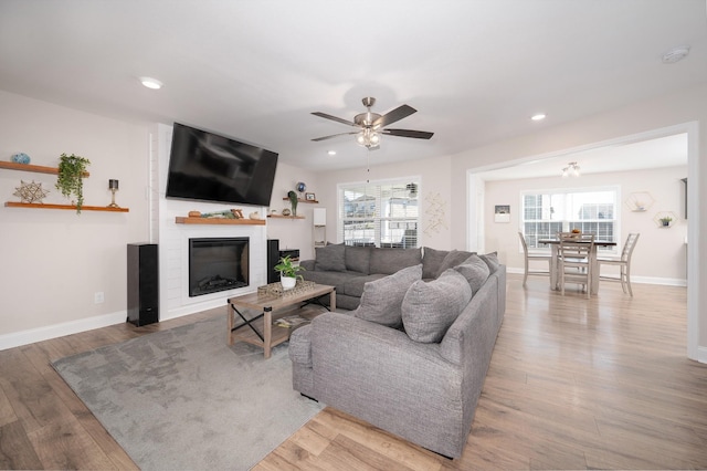 living room featuring plenty of natural light, a glass covered fireplace, light wood-style flooring, and baseboards