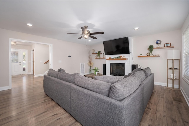 living area with a glass covered fireplace, visible vents, baseboards, and wood finished floors