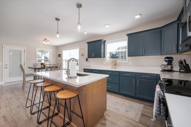 kitchen featuring pendant lighting, light countertops, a kitchen island with sink, a sink, and blue cabinets