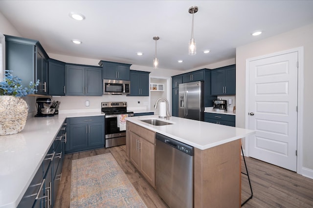 kitchen featuring stainless steel appliances, light countertops, a sink, and an island with sink