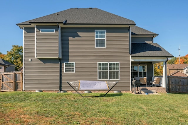 back of property with a shingled roof, fence, a patio, and a yard