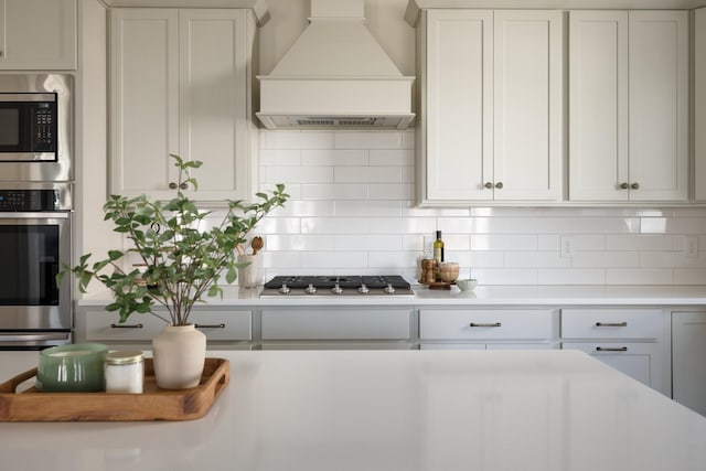 kitchen featuring white cabinets, appliances with stainless steel finishes, custom exhaust hood, light countertops, and backsplash