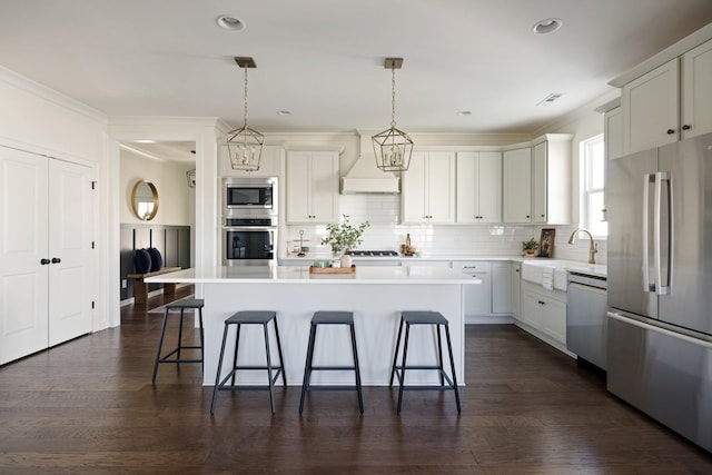 kitchen featuring custom exhaust hood, light countertops, appliances with stainless steel finishes, a kitchen island, and a kitchen bar