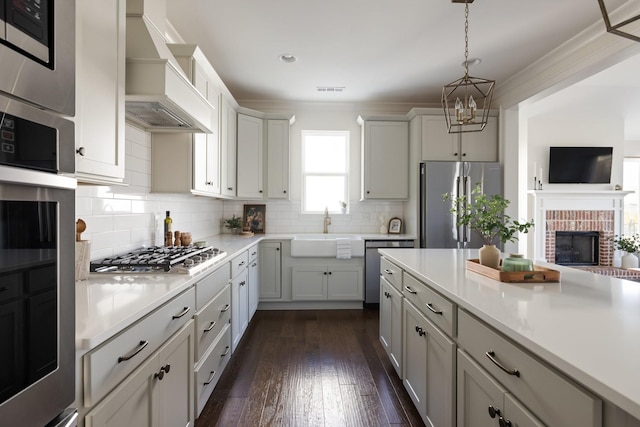 kitchen featuring decorative light fixtures, stainless steel appliances, light countertops, a sink, and premium range hood