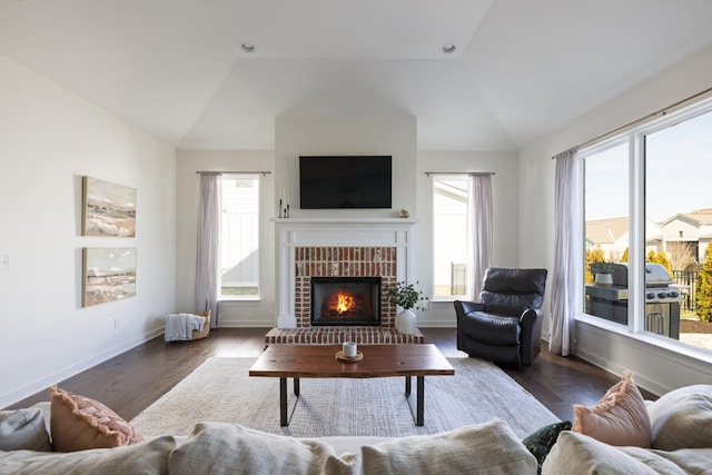 living area featuring lofted ceiling, a brick fireplace, baseboards, and wood finished floors