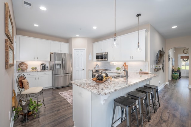 kitchen with arched walkways, pendant lighting, appliances with stainless steel finishes, white cabinetry, and a peninsula