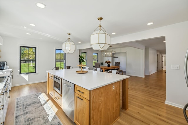 kitchen with a kitchen island, appliances with stainless steel finishes, decorative light fixtures, light countertops, and light wood-style floors