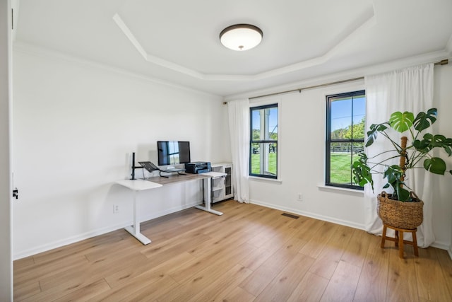 office with light wood finished floors, visible vents, baseboards, a raised ceiling, and crown molding