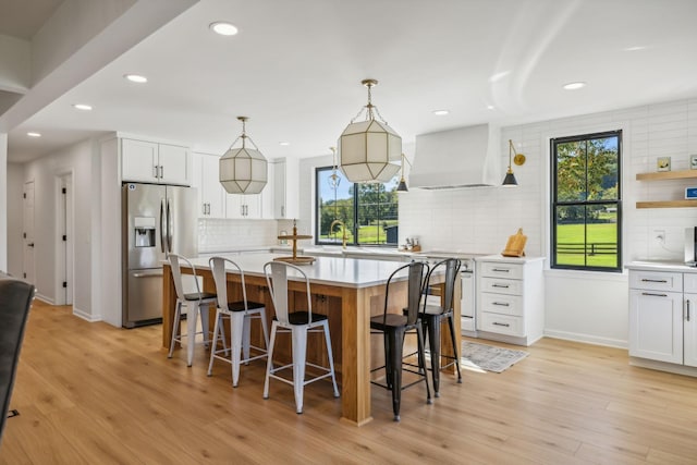 kitchen featuring premium range hood, a kitchen island, white cabinets, stainless steel fridge, and decorative light fixtures