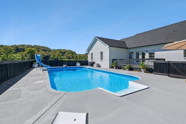 view of swimming pool with a deck, a patio, a water slide, fence, and a fenced in pool