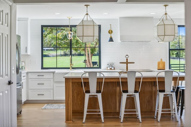 kitchen featuring a kitchen island, white cabinets, light countertops, a kitchen bar, and pendant lighting