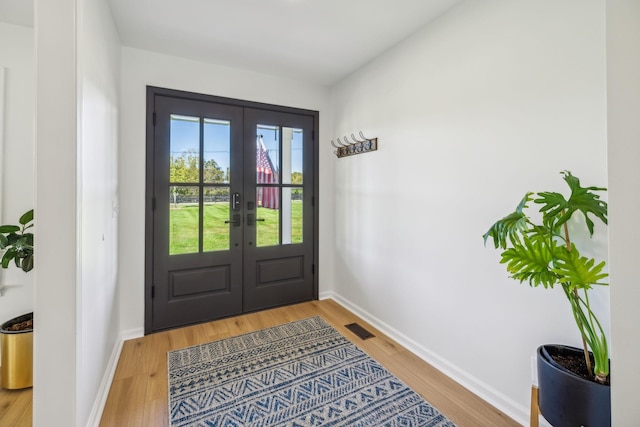 doorway with light wood finished floors, baseboards, visible vents, and french doors