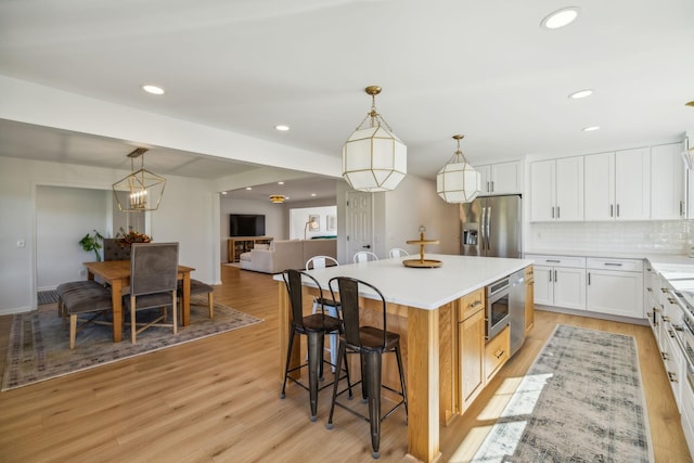 kitchen with white cabinets, appliances with stainless steel finishes, a center island, hanging light fixtures, and light countertops