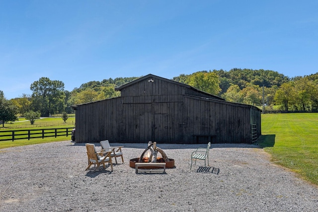 view of barn featuring a rural view, fence, a fire pit, and a yard