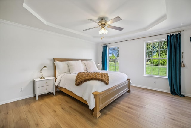 bedroom with light wood-style flooring, baseboards, and a raised ceiling