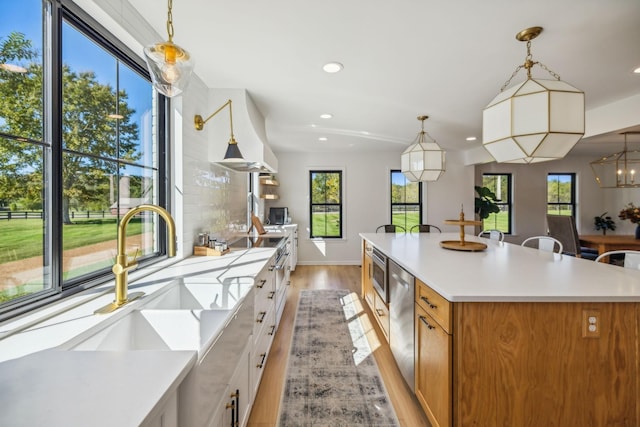 kitchen featuring a spacious island, light countertops, a sink, and wall chimney exhaust hood