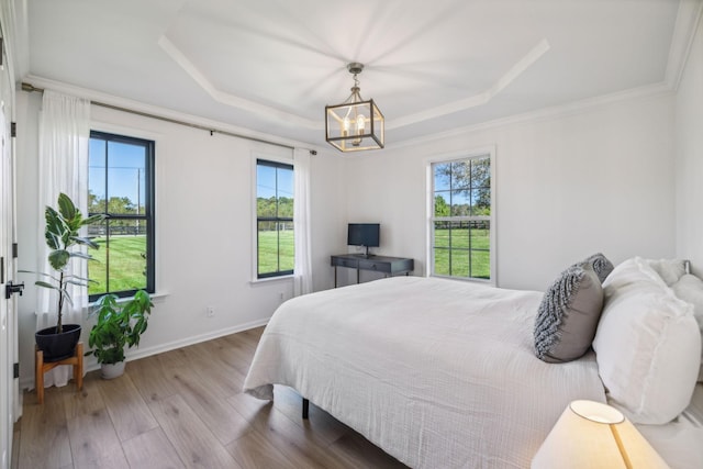 bedroom featuring a notable chandelier, baseboards, light wood-style floors, a tray ceiling, and crown molding