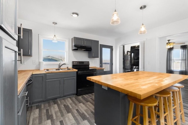 kitchen with black / electric stove, under cabinet range hood, butcher block counters, stacked washing maching and dryer, and a center island