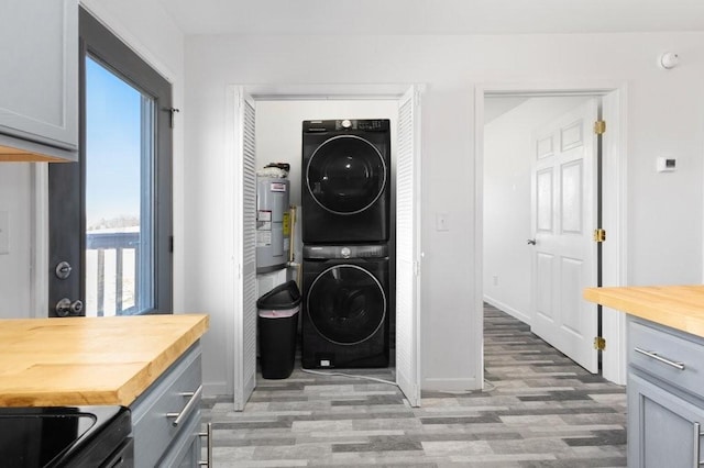 clothes washing area with electric water heater, stacked washer and dryer, laundry area, and light wood-style floors