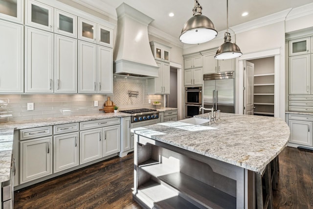 kitchen with premium range hood, a kitchen island with sink, glass insert cabinets, and stainless steel appliances