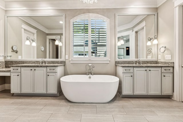 bathroom featuring ornamental molding, two vanities, a freestanding bath, and a sink