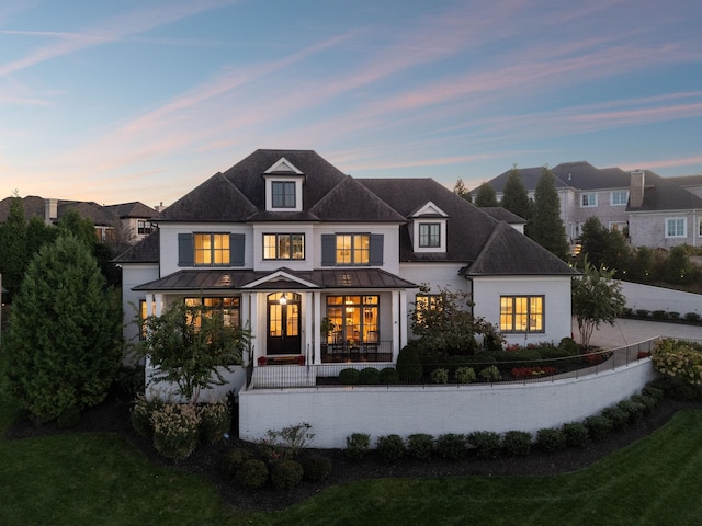 back of house at dusk with covered porch, a yard, a standing seam roof, and metal roof