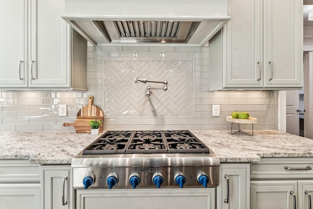 kitchen with premium range hood, backsplash, light stone countertops, and stainless steel gas stovetop