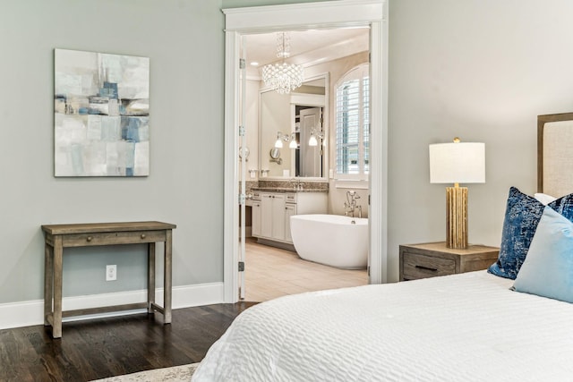 bedroom featuring a notable chandelier, baseboards, wood finished floors, and ensuite bathroom