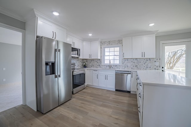 kitchen with stainless steel appliances, white cabinetry, a sink, and ornamental molding