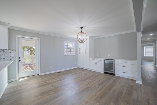 kitchen featuring light wood finished floors, beverage cooler, white cabinets, ornamental molding, and light countertops