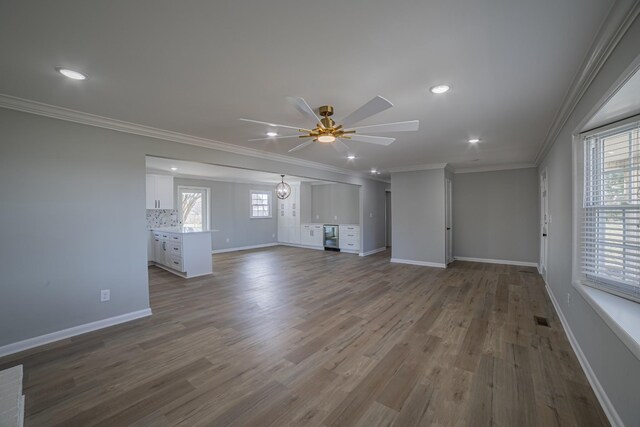 unfurnished living room featuring ceiling fan, a healthy amount of sunlight, wood finished floors, and crown molding