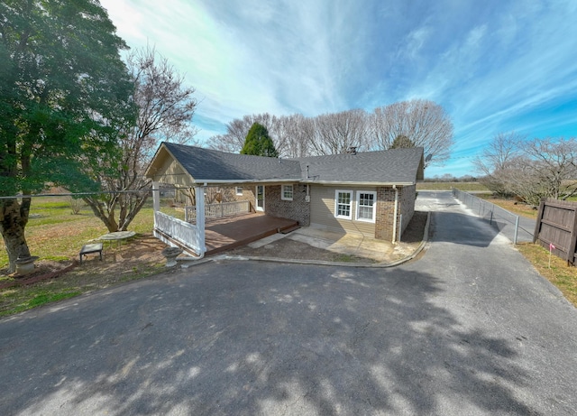 single story home featuring aphalt driveway, roof with shingles, fence, a deck, and brick siding