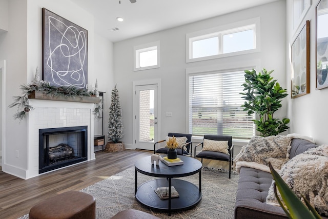 living area featuring visible vents, baseboards, a tiled fireplace, dark wood-style flooring, and a high ceiling