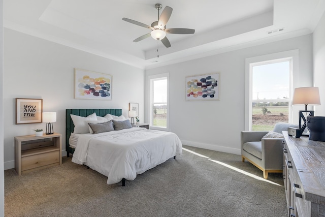 carpeted bedroom featuring ceiling fan, a tray ceiling, visible vents, and baseboards