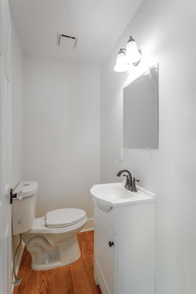 bathroom with visible vents, toilet, vanity, wood finished floors, and baseboards