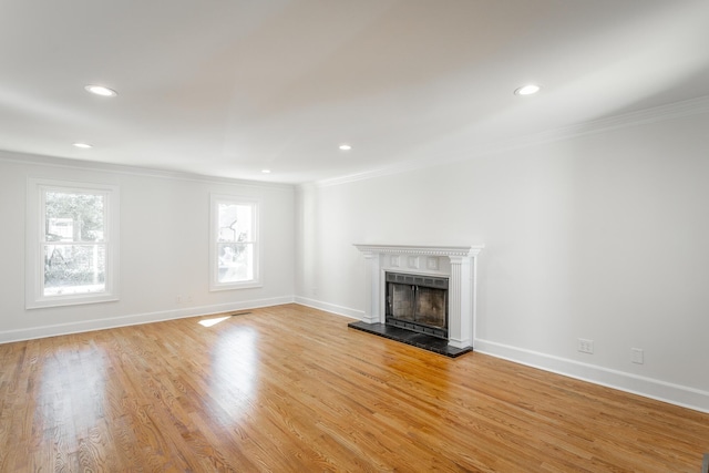 unfurnished living room featuring recessed lighting, a fireplace with raised hearth, light wood-style floors, ornamental molding, and baseboards