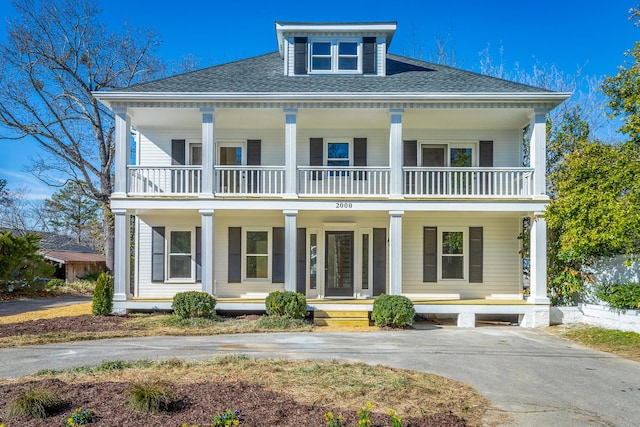 greek revival inspired property featuring a porch, a shingled roof, and a balcony