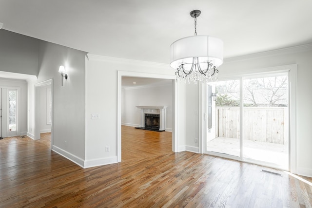 unfurnished dining area with a chandelier, a fireplace with raised hearth, dark wood finished floors, and crown molding